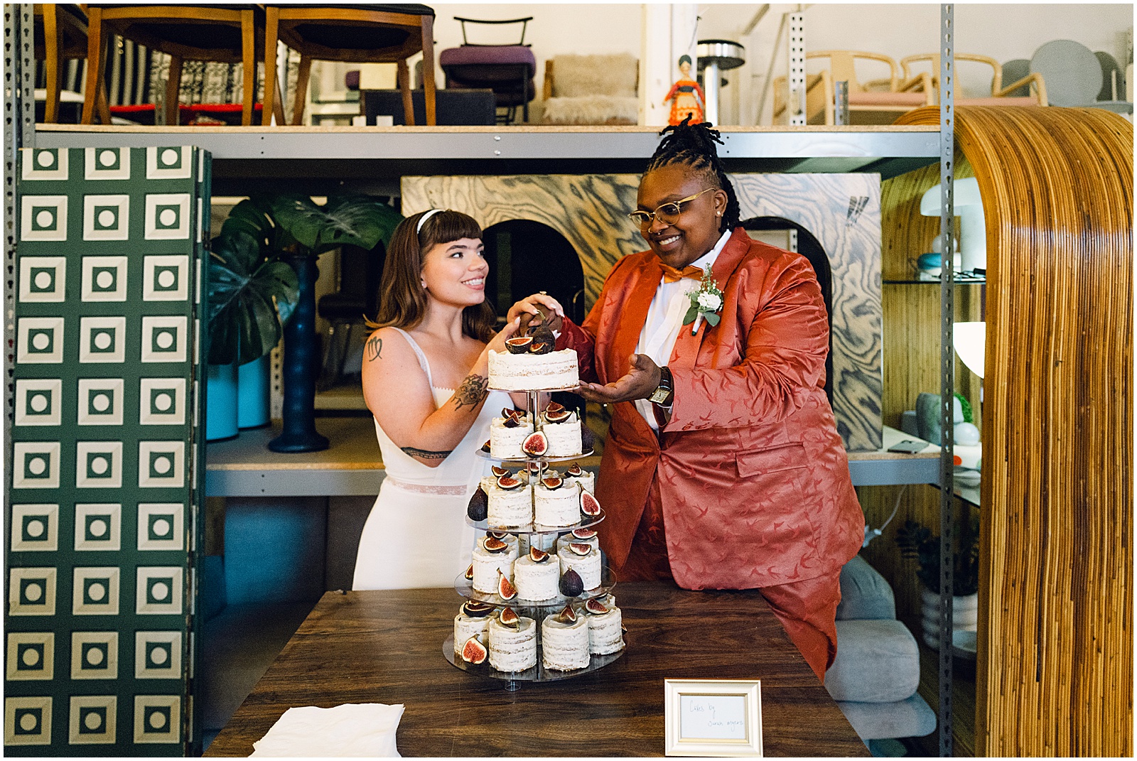 Two brides laugh as they cut a tiered wedding cake in a Philadelphia wedding venue.