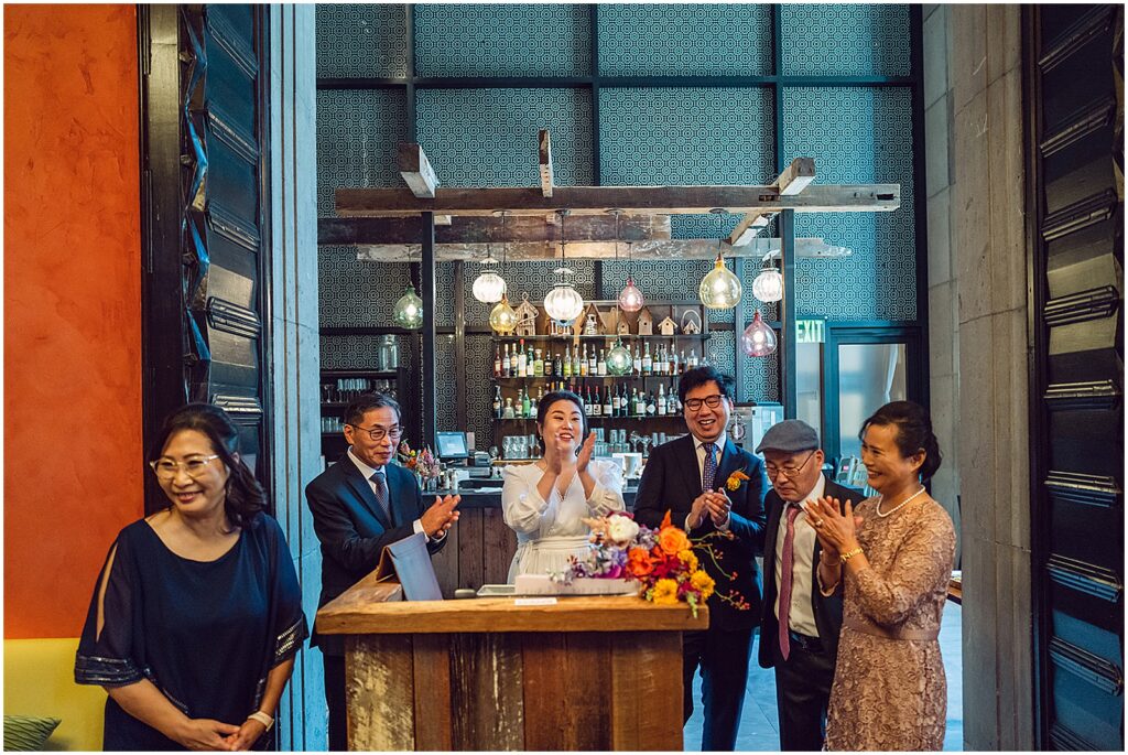 A bride and groom's parents stand with them during a ceremony in a restaurant wedding venue.