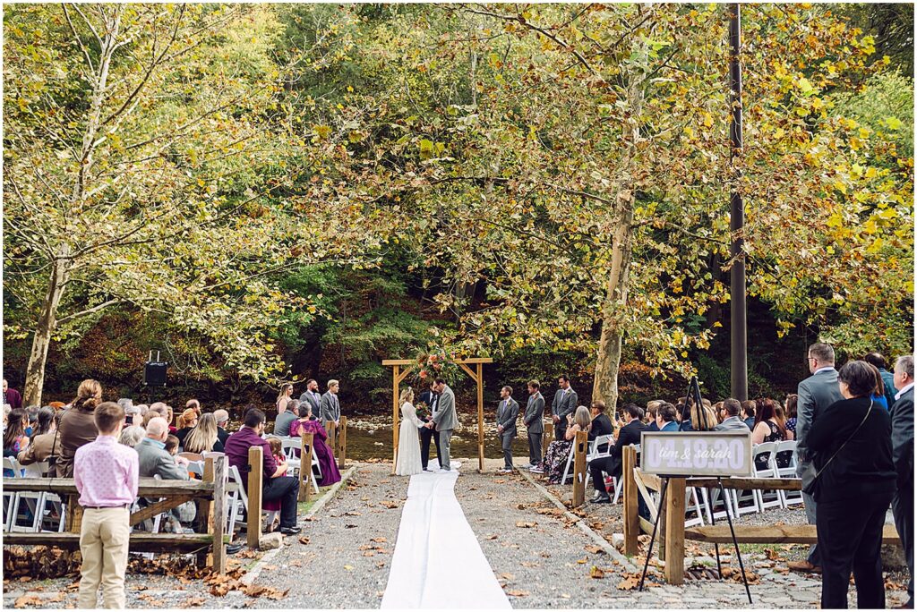 A bride and groom stand for a creekside wedding ceremony at a restaurant wedding venue in Philly.