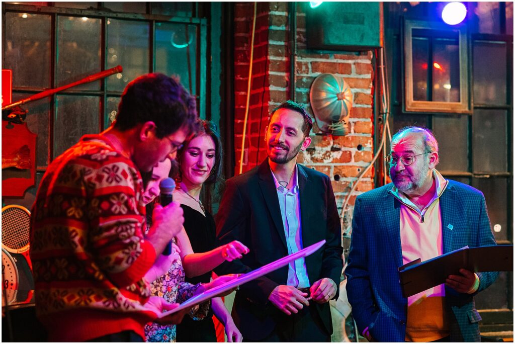 A person reads a speech into a microphone as a bride and groom look on.