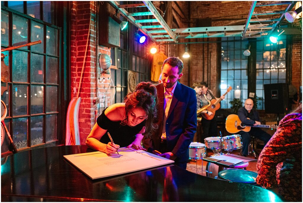 A bride signs a ketubah on a stage.