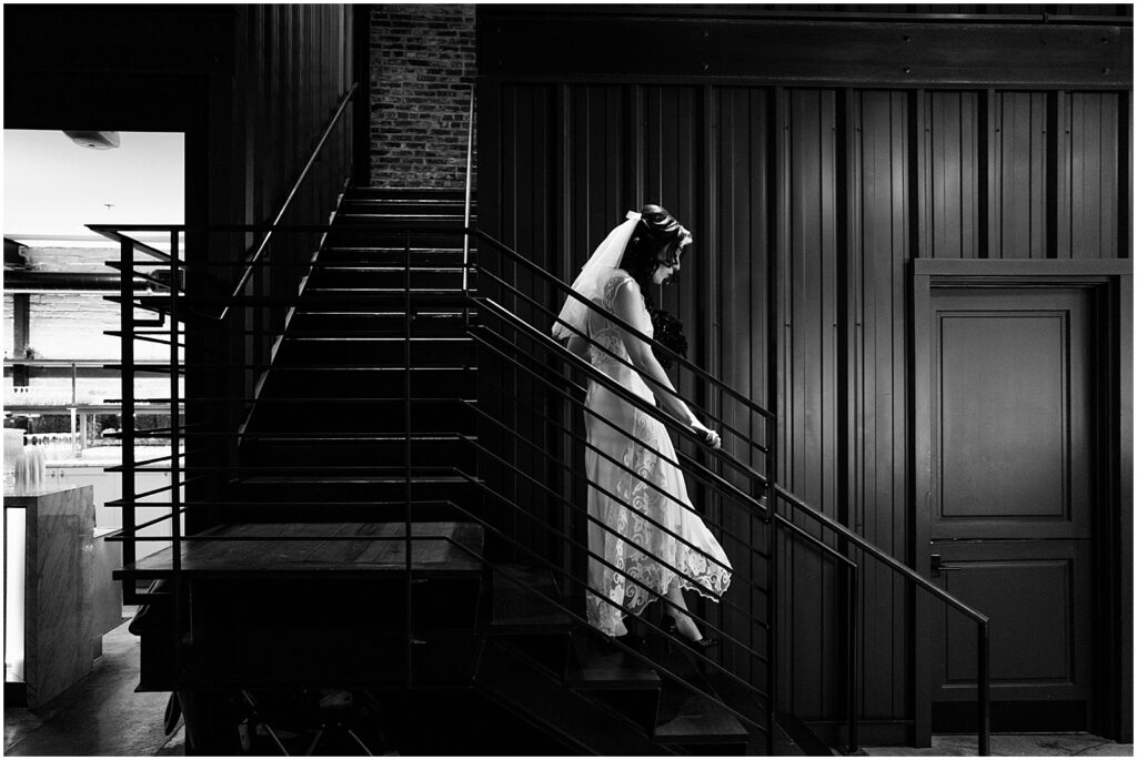 A bride walks down a staircase in a black and white wedding photo.