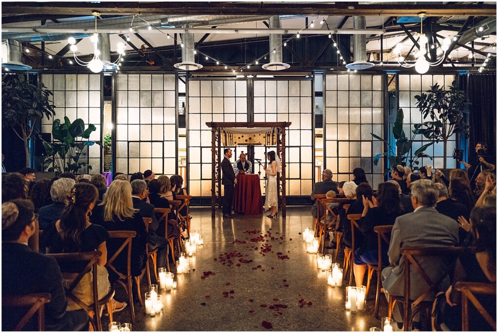 A bride and groom stand beneath a chuppah at a candlelit wedding ceremony in Lilah Philadelphia.