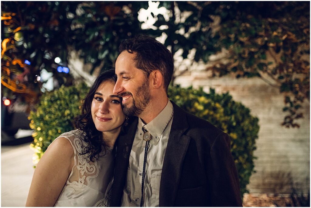 A bride leans on a groom's shoulder at night.