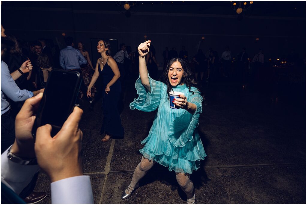 A wedding guest in a blue dress dances with a cocktail.