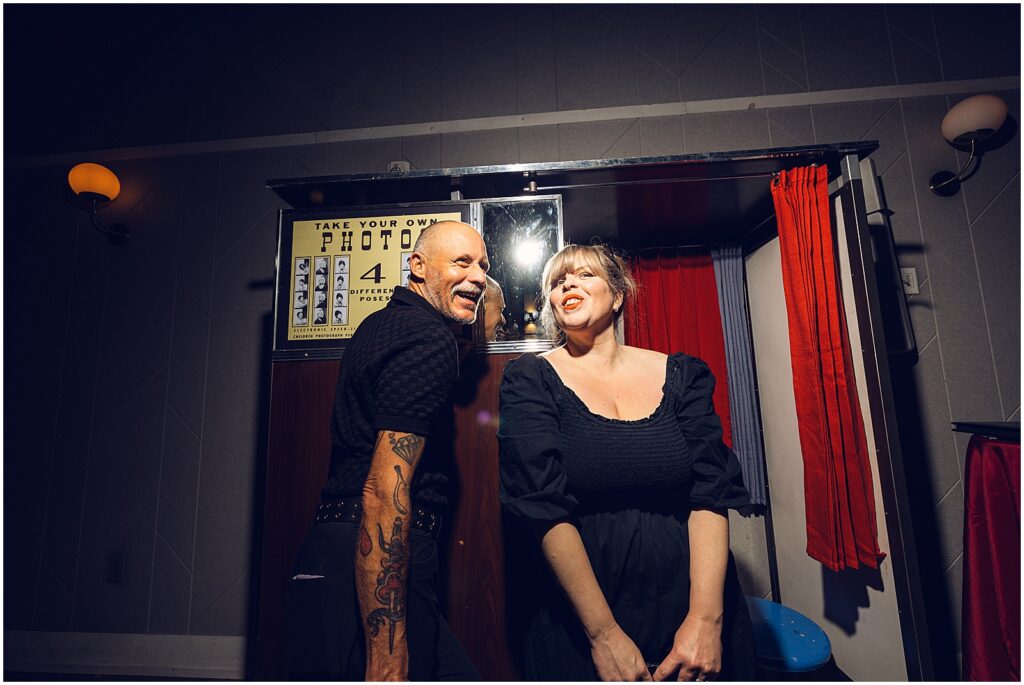 Two wedding guests sing beside a photobooth.
