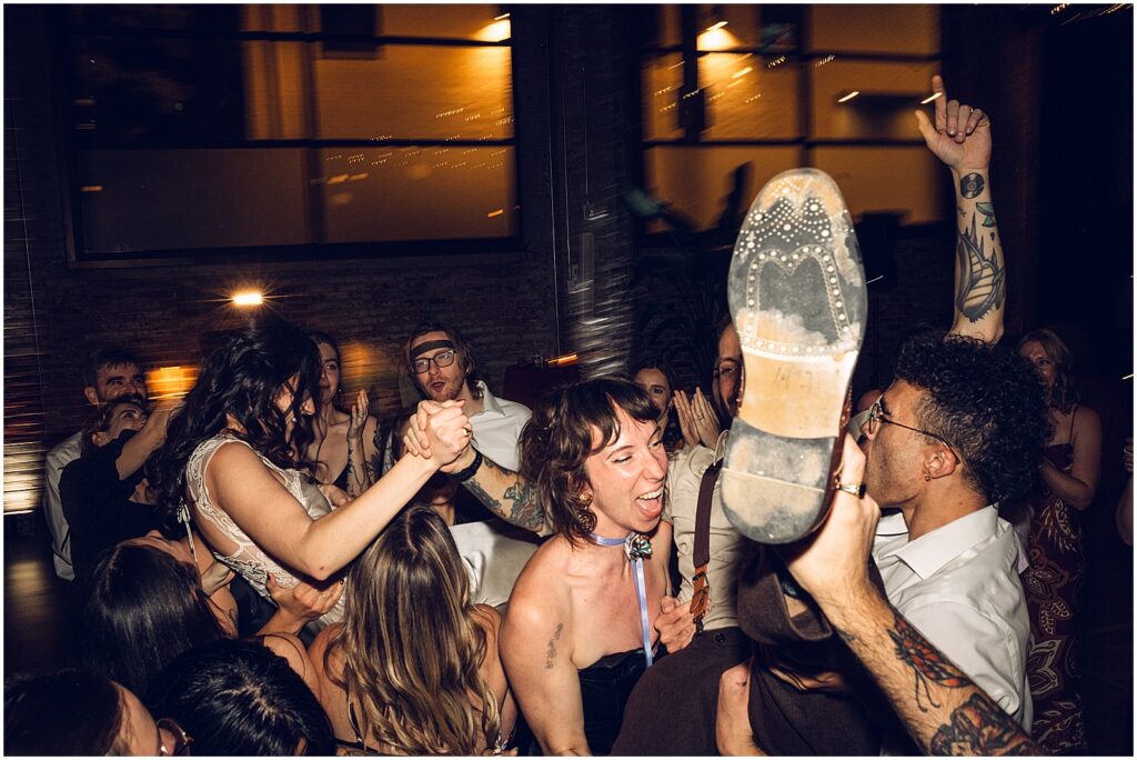Wedding guests lift up a groom on the dance floor.