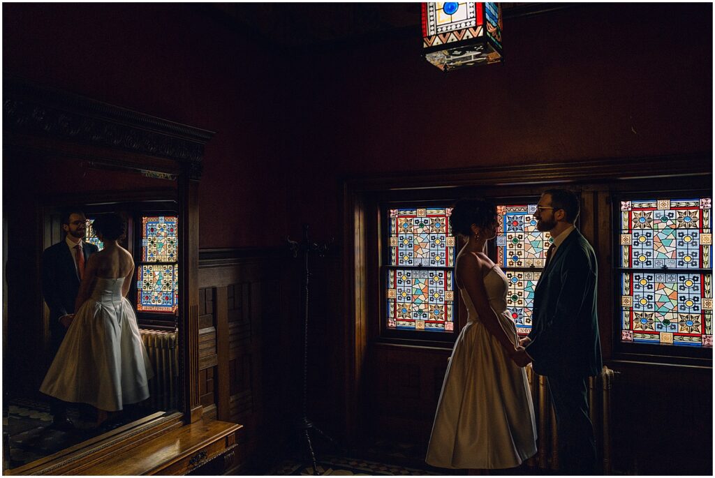 A bride and groom pose for a Philly wedding photographer beside stained glass windows.