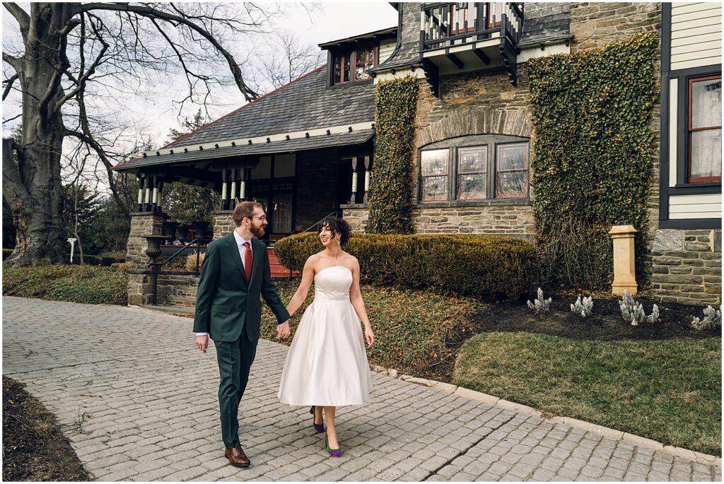 A bride and groom hold hands and walk down a Philly sidewalk in the winter.