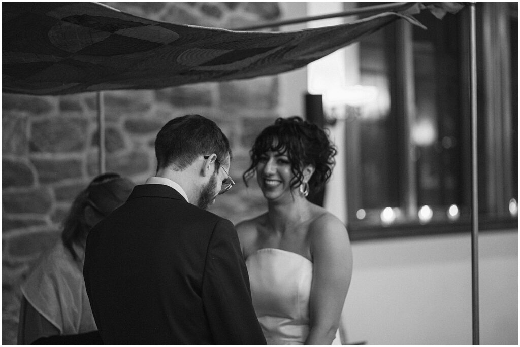 A bride smiles at a groom during a wedding ceremony.