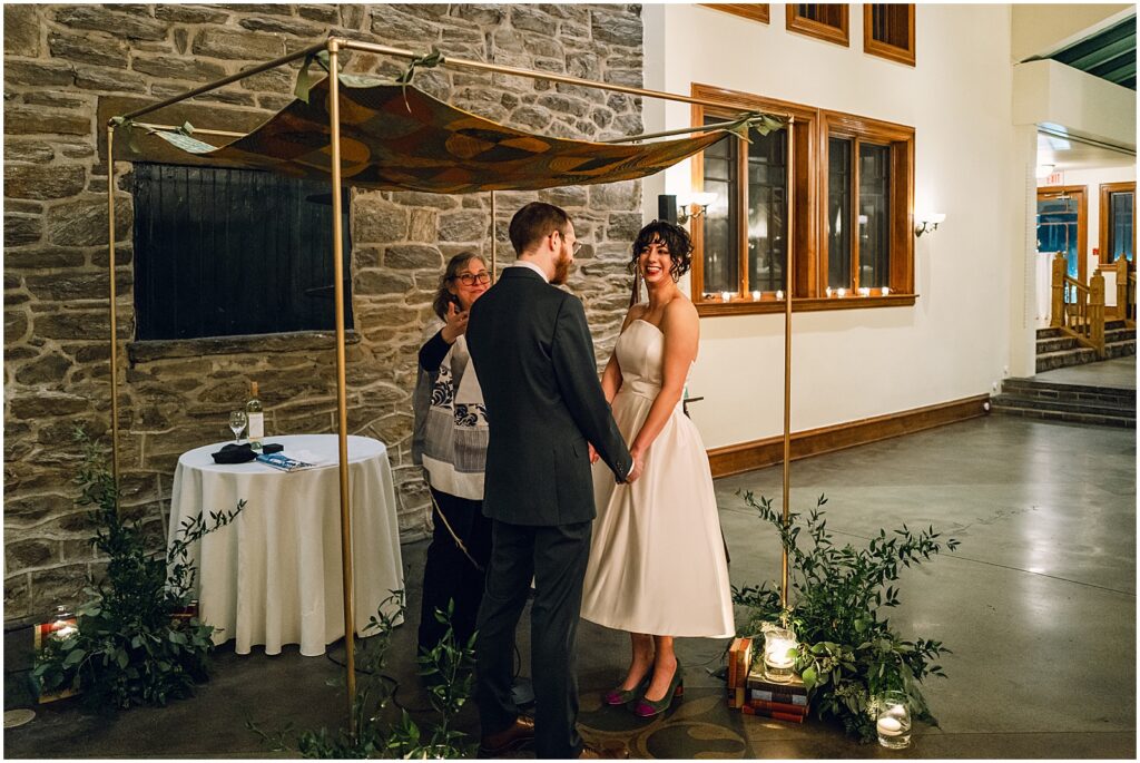 A bride and groom smile beside a chuppah at Knowlton Mansion.