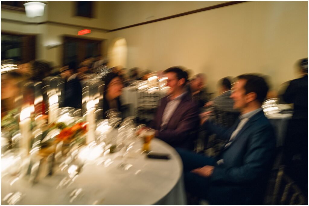A blurry photo shows guests talking at a reception table.