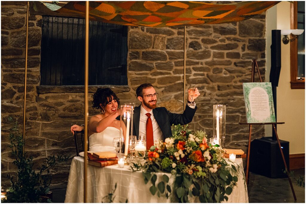 A bride and groom raise their glasses at their sweetheart table in Knowlton Mansion.