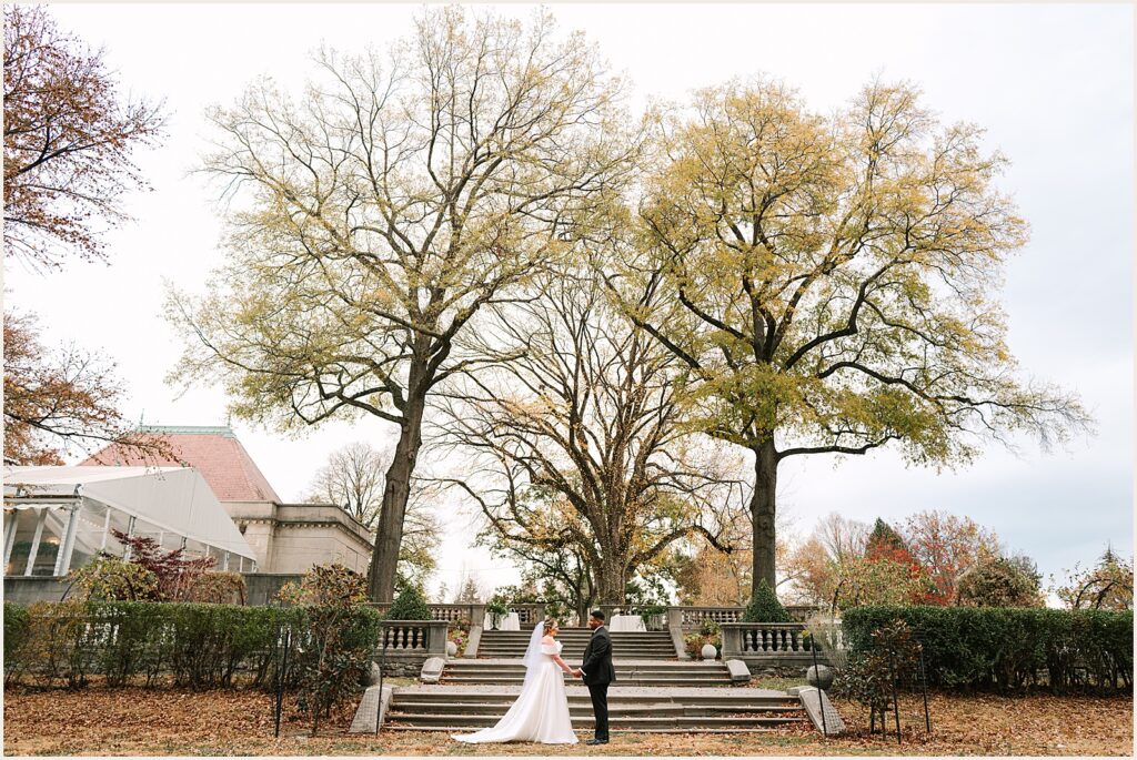 A bride and groom walk through the arboretum outside Curtis Hall in fall.