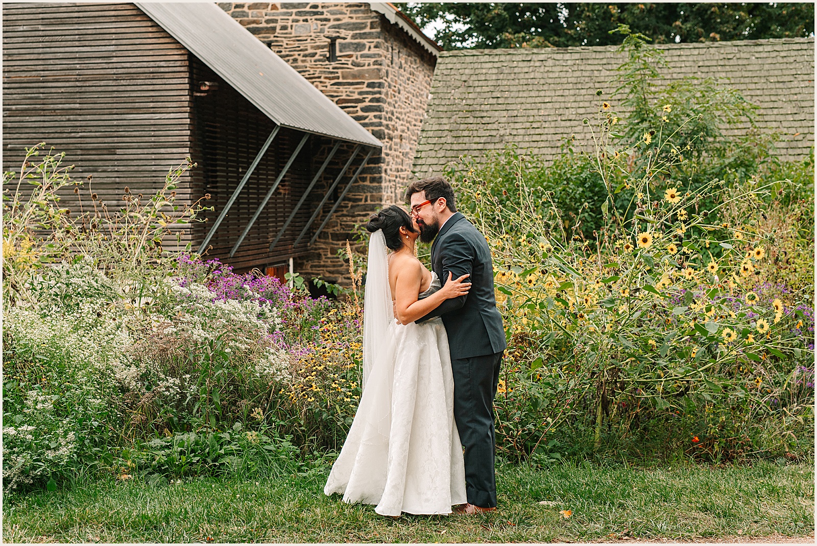 A bride and groom kiss outside a barn at Bartram's Garden.