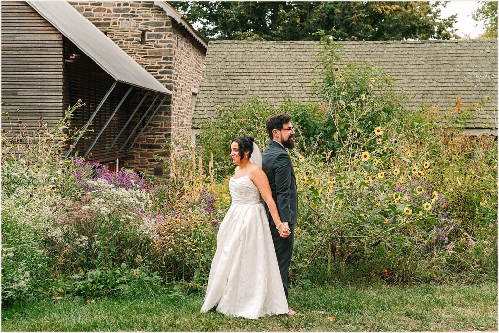 A bride and groom stand back to back at a garden wedding venue.