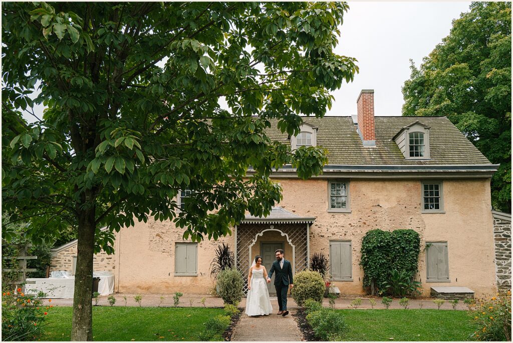 A bride and groom pose in front of a historic house at Bartram's Garden.