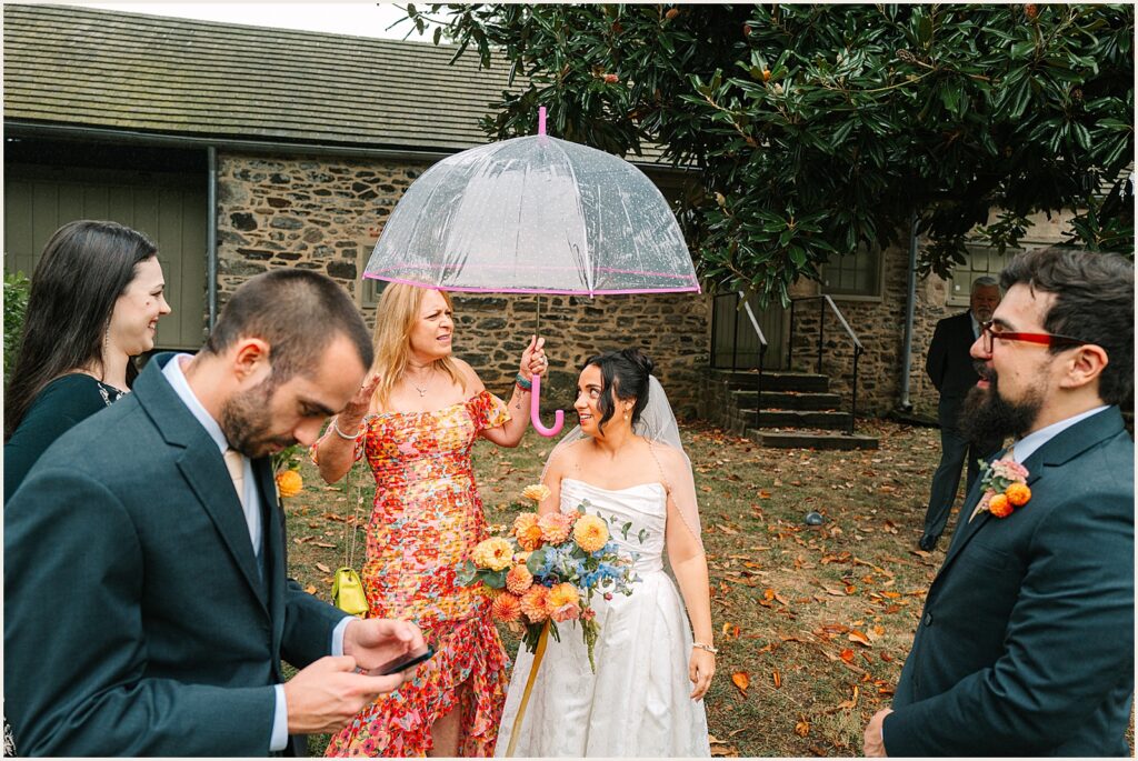 A wedding guest holds an umbrella over a bride.