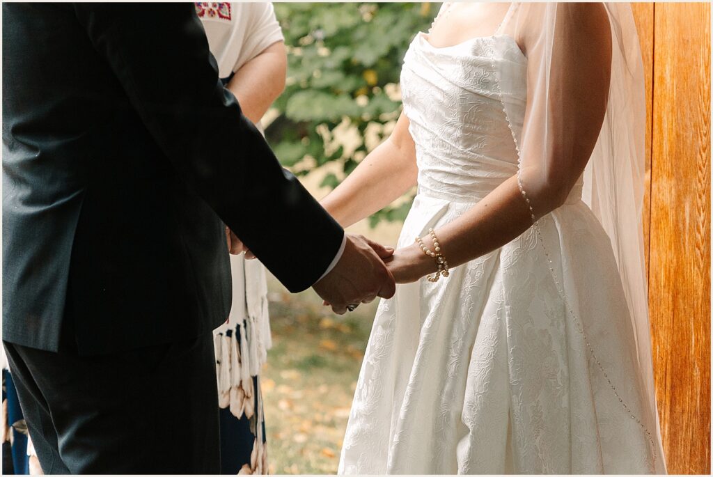 A bride and groom hold hands while they talk to a rabbi.