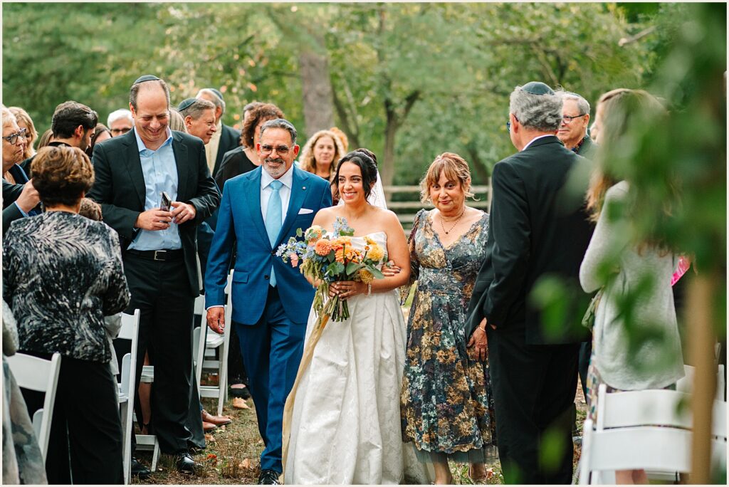 A bride walks up the aisle with her mother and father.