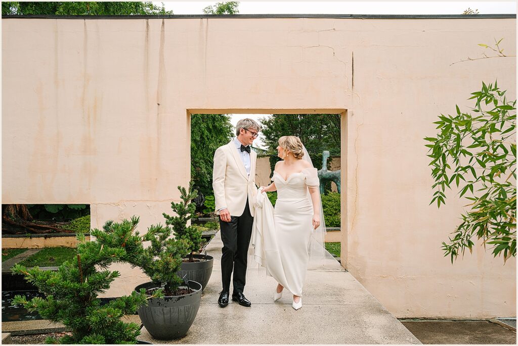 A bride and groom pose in front of a doorway leading to a sculpture garden.