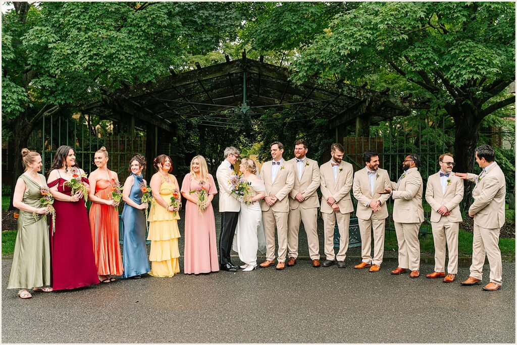 A bride and groom pose with their wedding party dressed in colorful clothes.