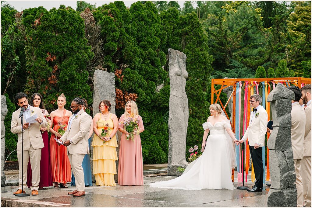 A bride and groom listen to a speech during a Grounds for Sculpture wedding ceremony.