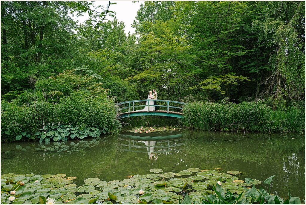 A bride and groom pose in the middle of a bridge at their Grounds for Sculpture wedding.