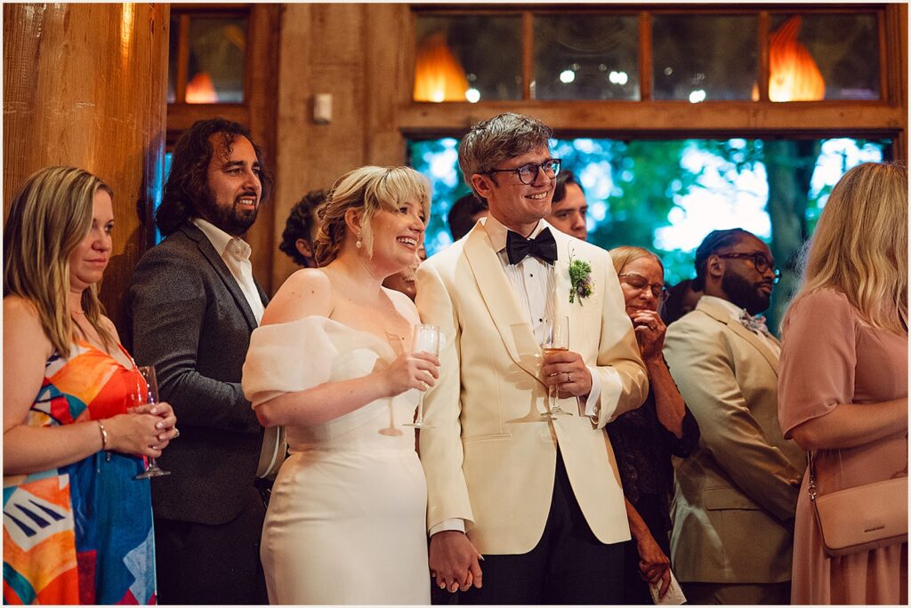 A bride and groom hold hands while they listen to a toast.