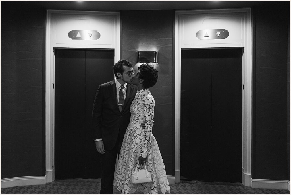 A bride and groom kiss in front of elevators.