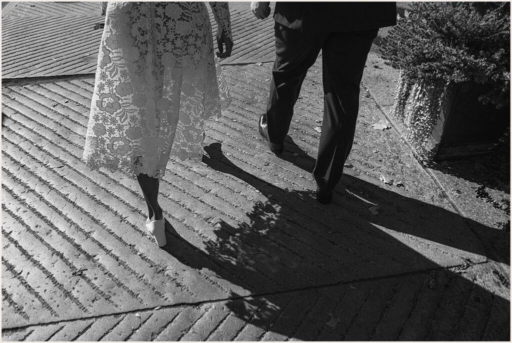A bride and groom walk down a brick sidewalk.