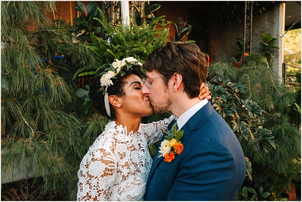 A bride and groom kiss beside a bush in Philadelphia.