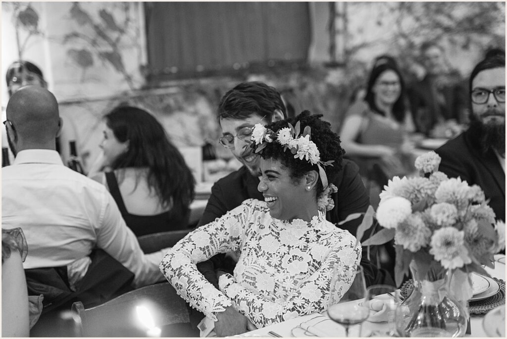 A bride leans against a groom to listen to a speech.