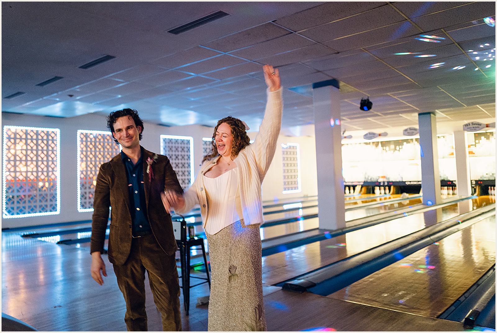 A bride and groom cheer at a bowling lane.