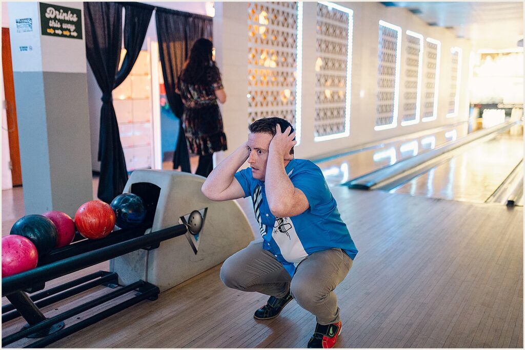 A wedding guest crouches on a bowling lane watching a ball roll.