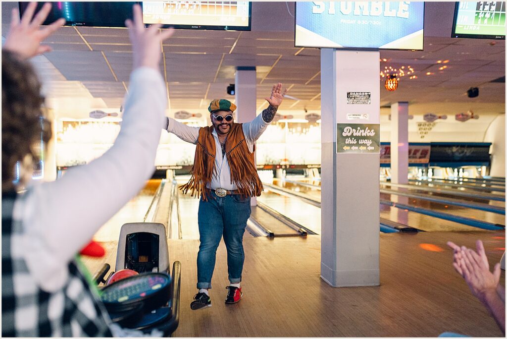 A wedding guest in a fringe vest cheers after bowling.