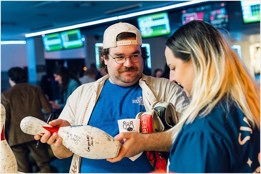 Wedding guests sign a bowling pin at a bowling wedding reception.