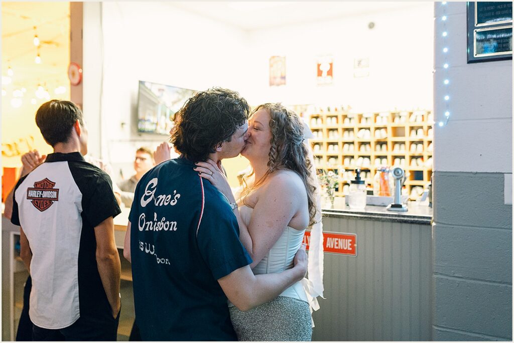 A bride and groom kiss beside the counter at a bowling alley reception.