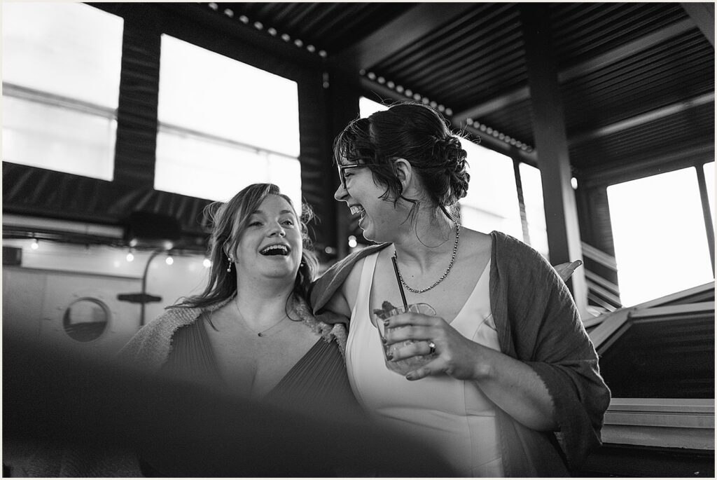 A bride puts an arm around a wedding guest's shoulders.