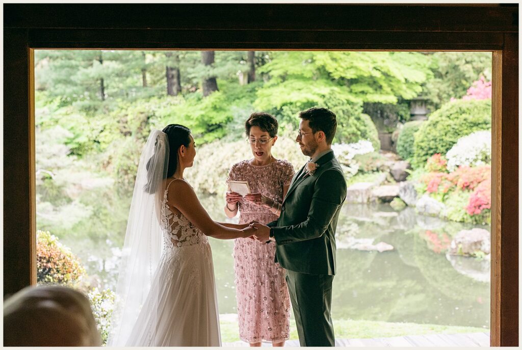 A bride and groom hold hands during a reading at their wedding ceremony.
