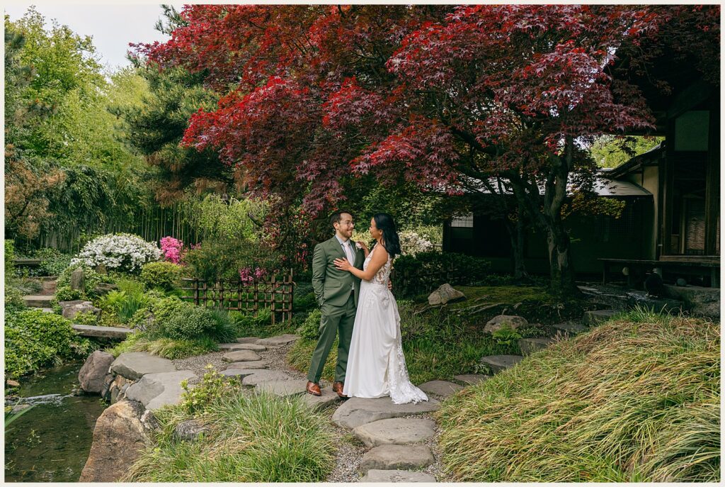 A bride and groom pose beside a Japanese maple.